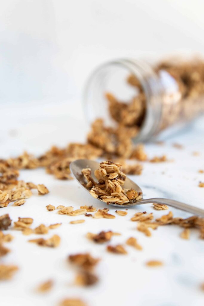 spilled jar of easy and healthy vegan and gluten-free granola with spoon next to it with granola on spoon