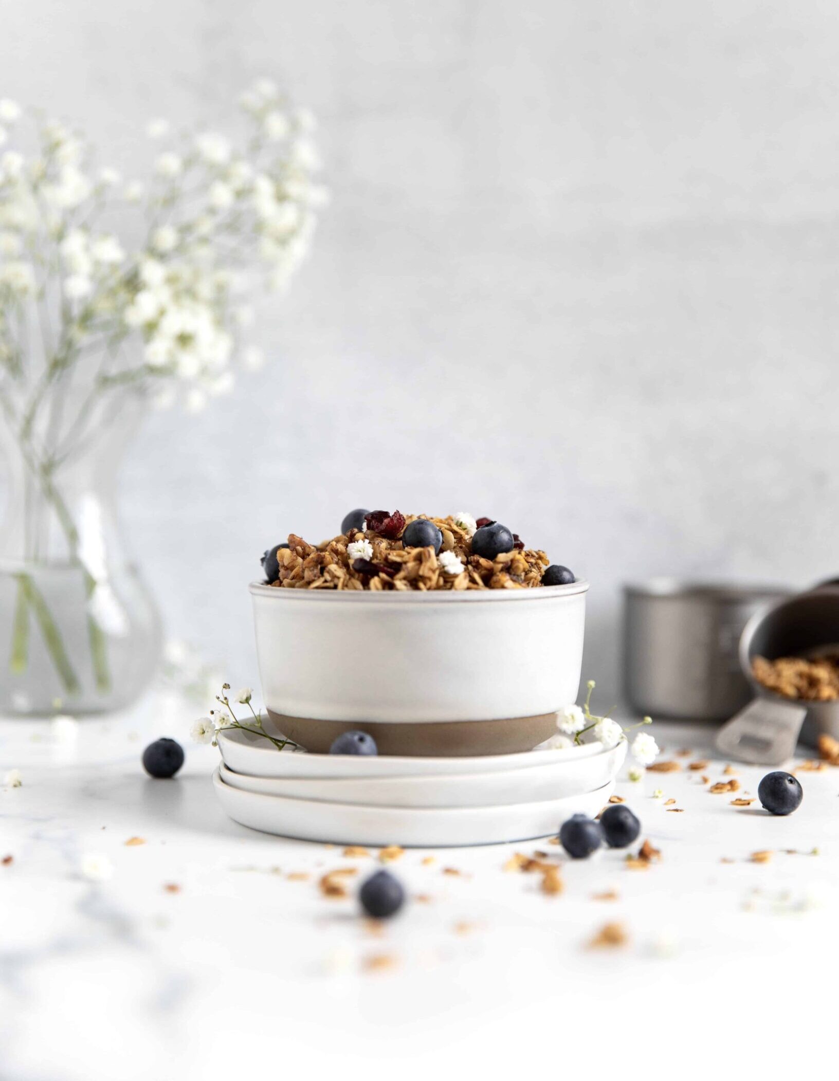 bowl of granola cereal with blueberries on top and flower vase in background