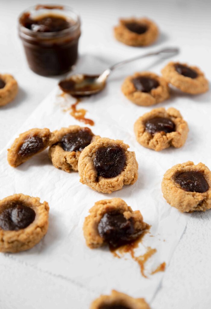 Easy vegan and gluten-free thumbprint cookies filled with apple butter with jar of apple butter in background and a spoon