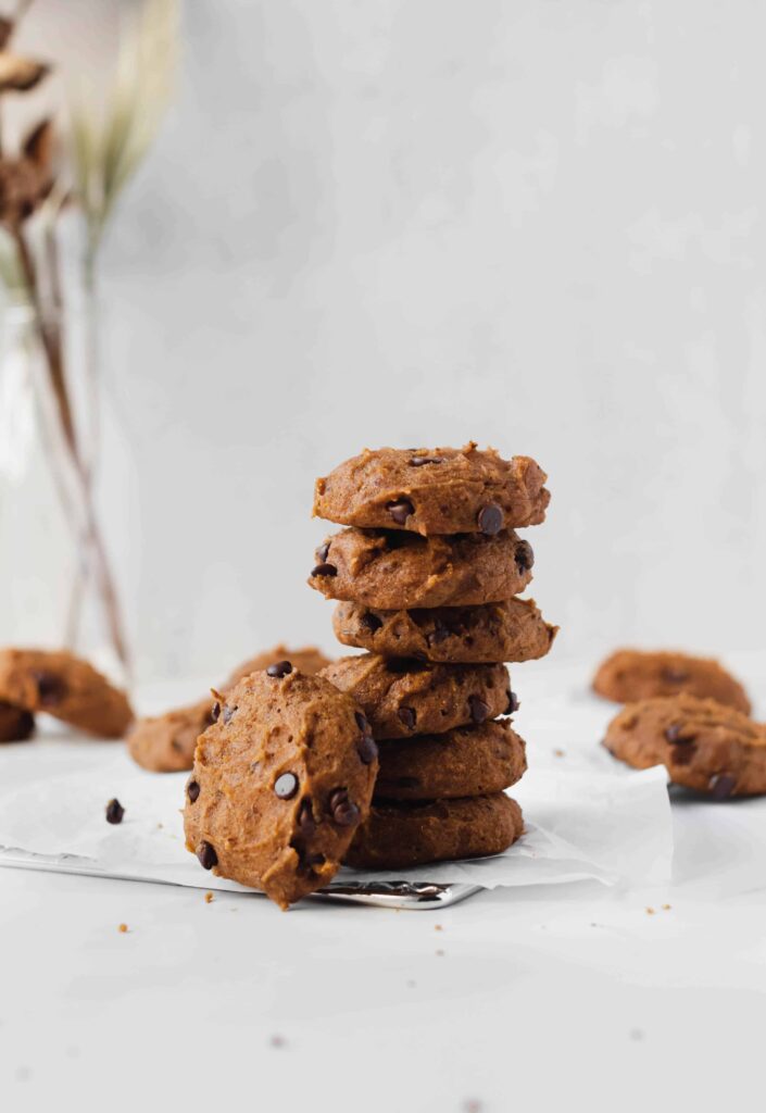 Stack of the best soft pumpkin chocolate chip cookies with cookies scattered in background and vase in background