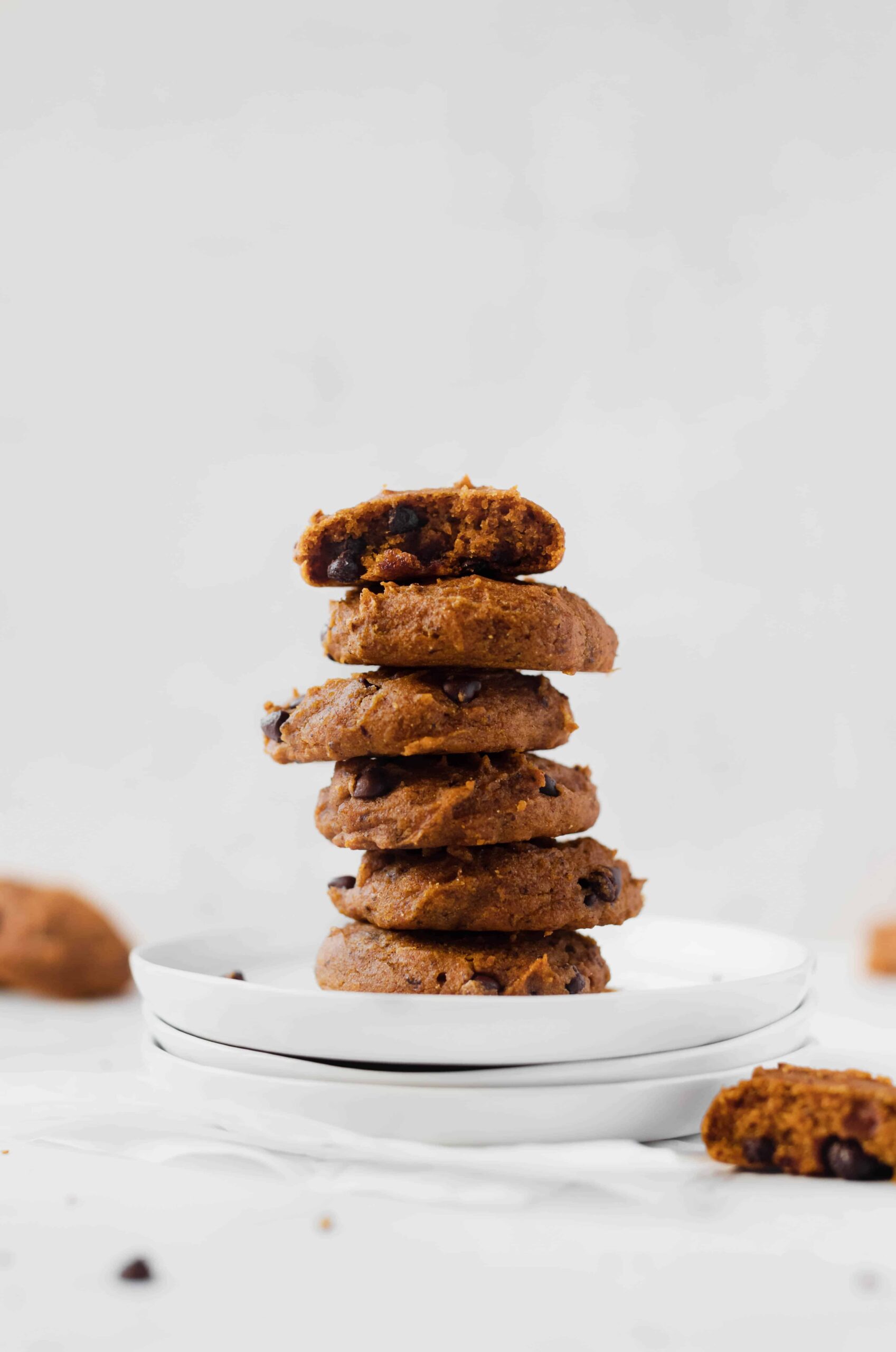 stack of soft pumpkin chocolate chip cookies on plate with cookies scattered in background